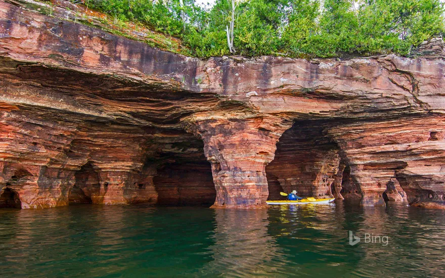 Kayaker exploring sandstone sea caves in Apostle Islands National Lakeshore near Bayfield, Wisconsin