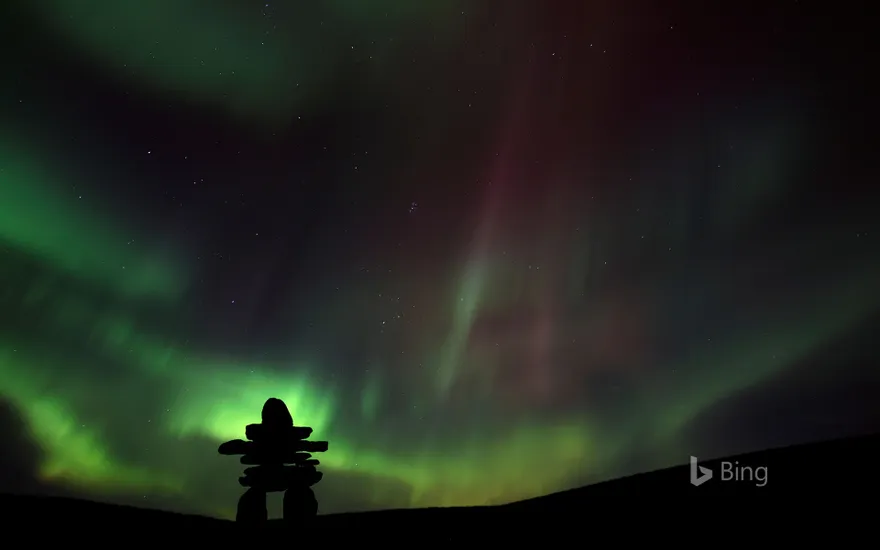 Inukshuk silhouetted against the northern lights in Barren Lands, Northwest Territories, Canada
