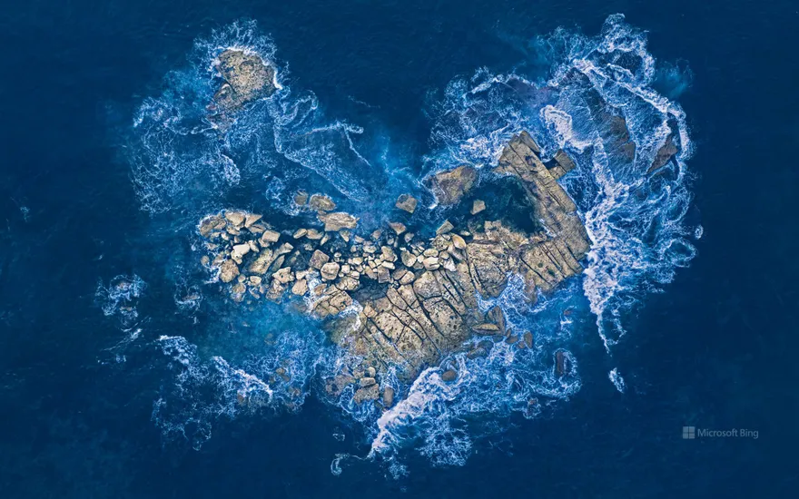 Ocean waves crashing over a heart-shaped rock island off the coast of Sydney, Australia