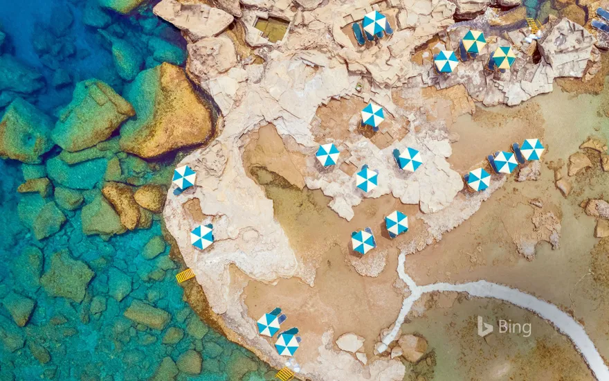 Aerial view of blue and white parasols on the rocky coast of Rhodes, an island in Greece